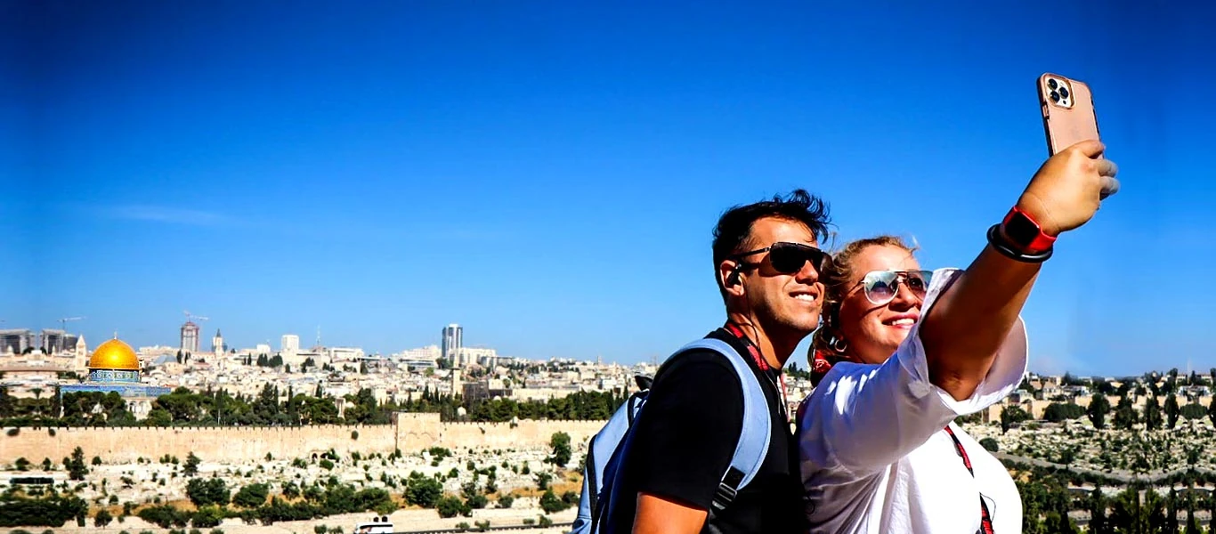Casal tirando foto no Monte das Oliveiras com vista para Jerusalém Casal de turistas registrando o momento no Monte das Oliveiras, com a cidade velha de Jerusalém ao fundo, incluindo a icônica Cúpula da Rocha