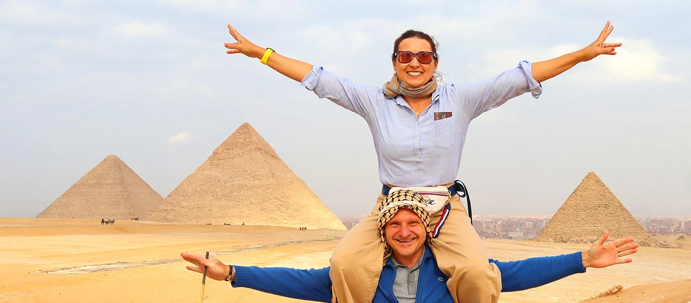 Casal feliz em frente as Pirâmides de Gizé A imagem mostra um casal de turistas em foto divertida nas Pirâmides de Gizé